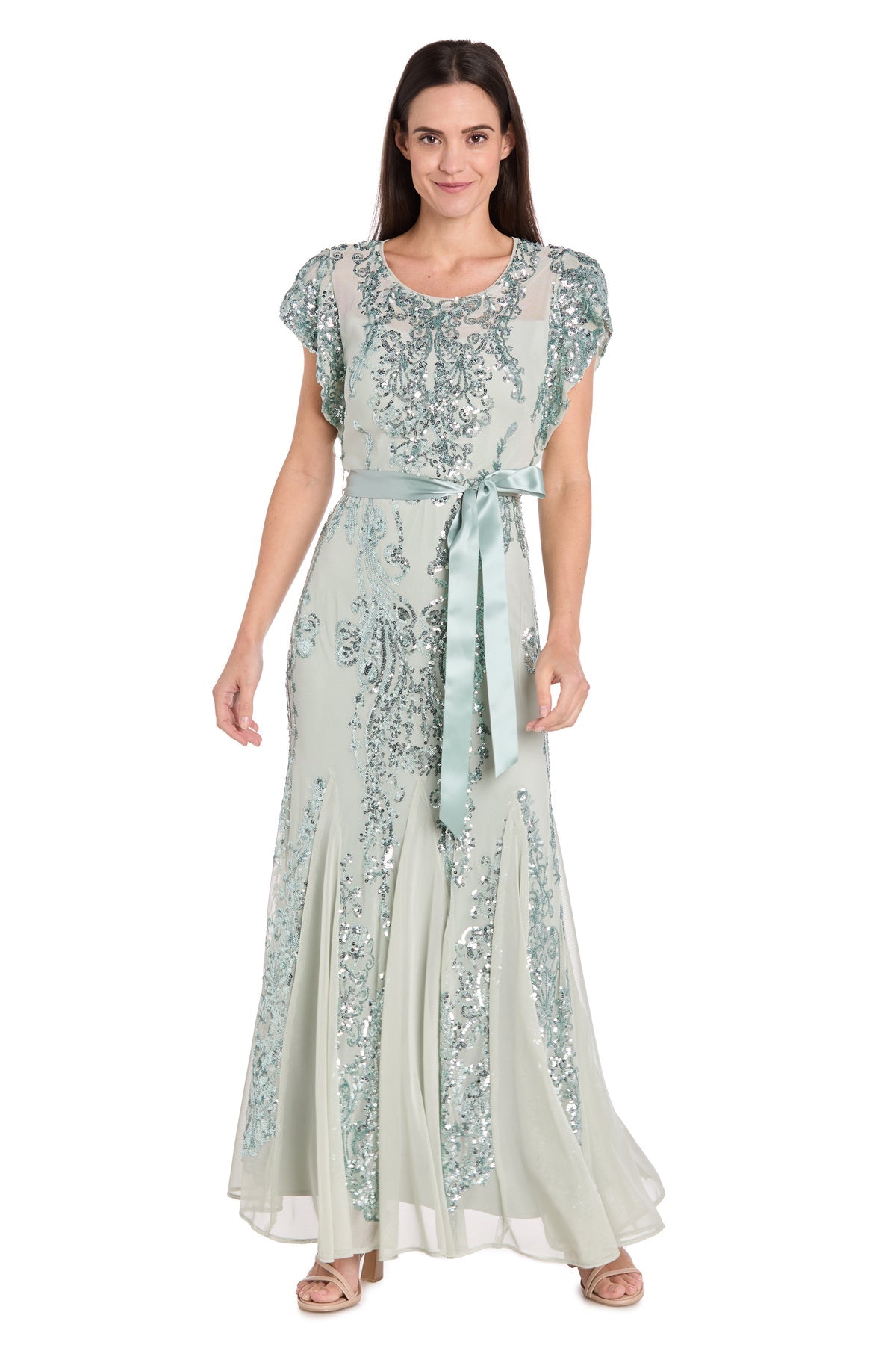 A woman wears the Petite Long Sage Formal Dress: R&M Richards 3465P, featuring sequin embellishments and a satin belt, standing against a white background.